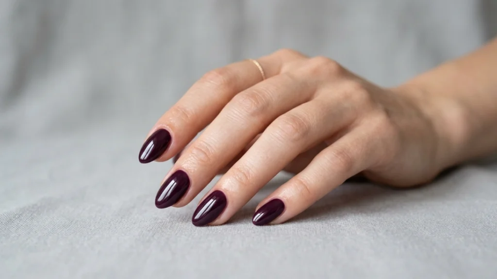 Dark plum nails styled on a short almond nail shape