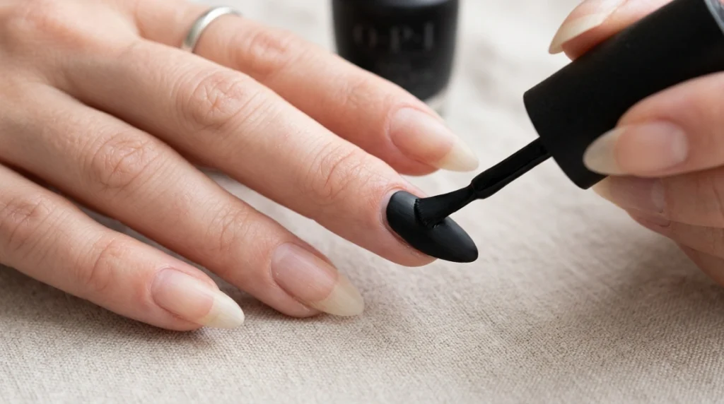 Matte black polish being applied to almond-shaped nails