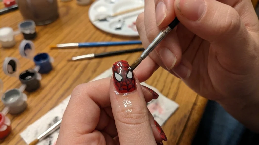 applying glossy top coat to finished red spiderweb nails